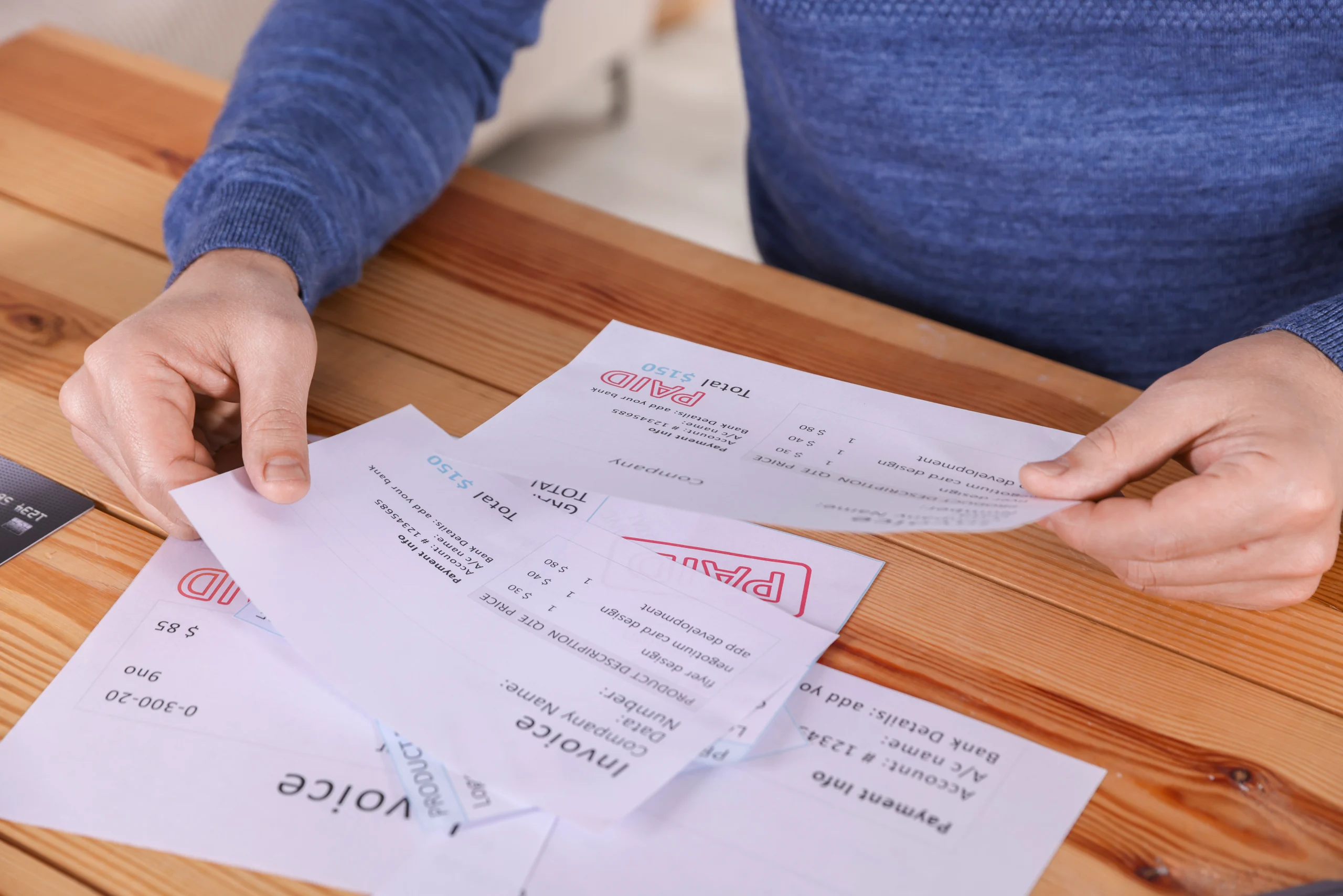 Paying bills. Man with invoices at wooden table indoors, closeup